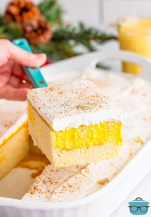 A freshly sliced piece of Eggnog Poke Cake held above the rest of the baking dish.