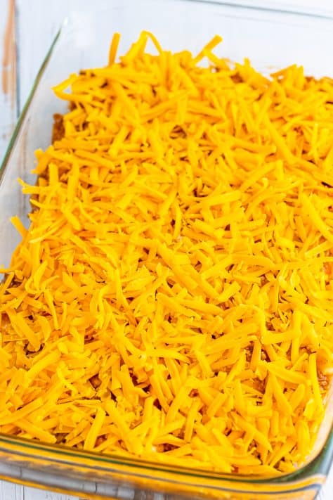Shredded cheese on top of the meat and biscuit mixture in a baking dish.