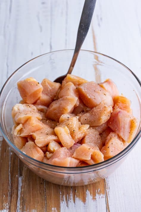 Diced chicken seasoned with salt and pepper in a glass mixing bowl.