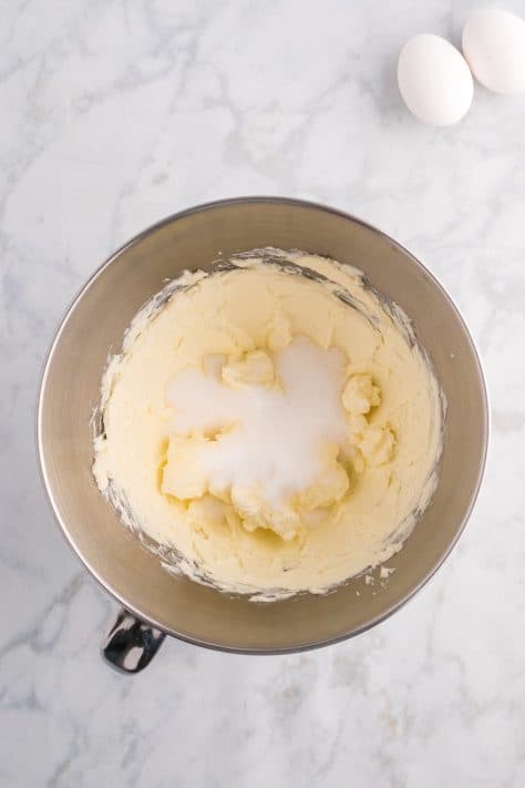 Sugar added to creamed butter and cream cheese in a mixing bowl.