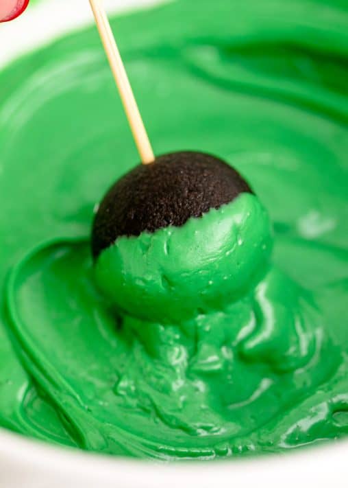 Green candy melted with a cookie ball being dipped in it.
