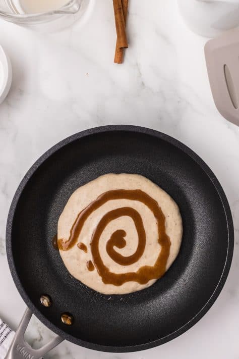 Pancake batter on a pan with cinnamon swirl.