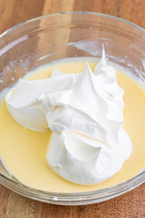 Whipped topping being added to a mixing bowl with cream cheese mixture.