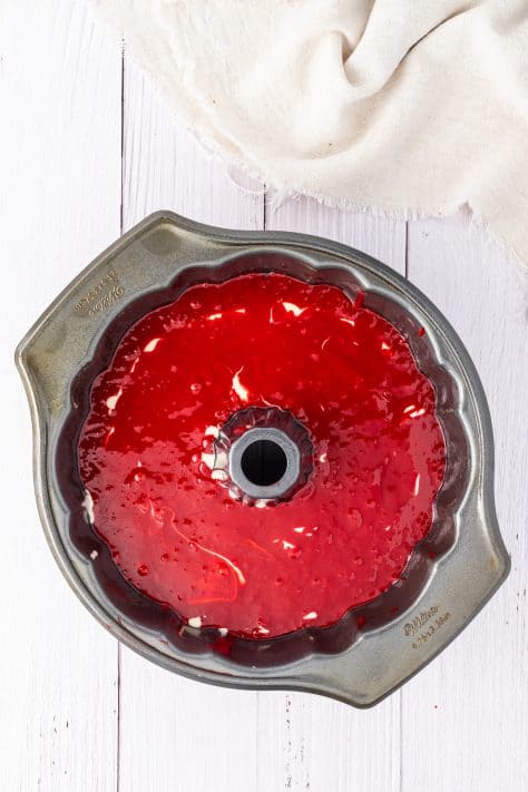 A bundt cake pan with half of the red velvet cake batter, cheesecake filling and the rest of the cake batter on top.