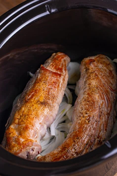 Seared pork tenderloins on a bed of onions in a Slow Cooker insert.