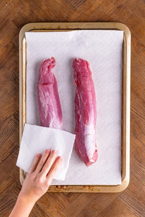 A hand patting pork tenderloins dry with paper towels.