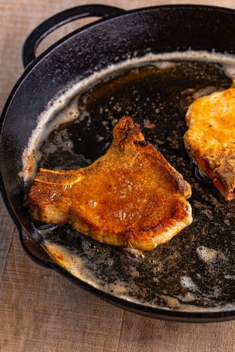 Seasoned and floured cooked pork chops in a pan.