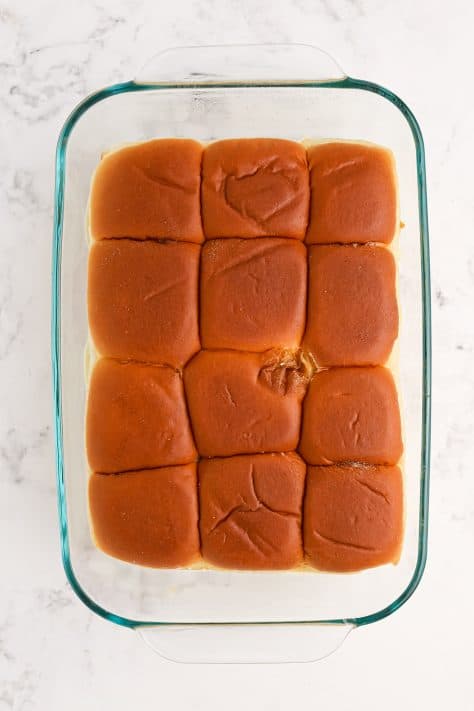 Slider rolls on top of sandwiches in a baking dish.