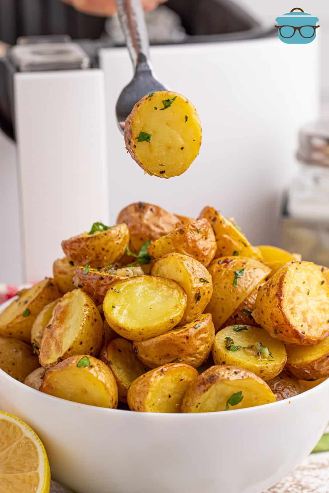 A utensil holding an Lemon Herb Potato over a serving bowl of them.