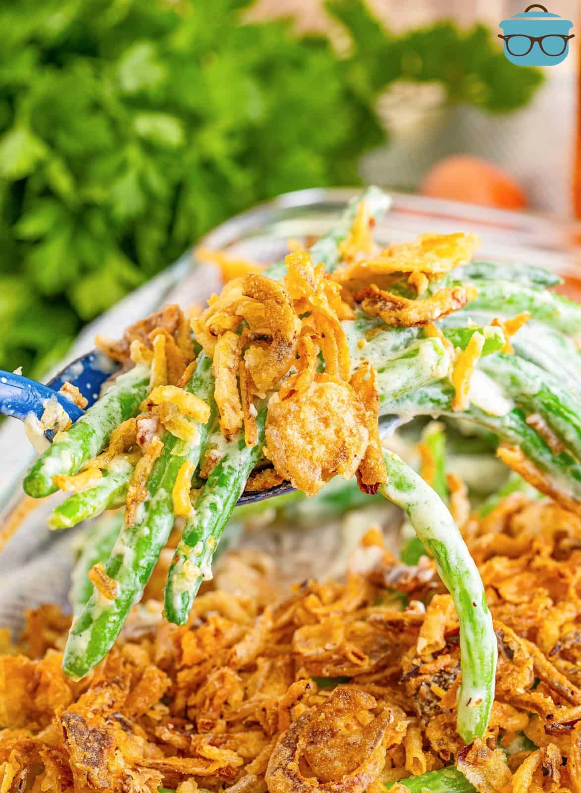 A scoop of Green Bean casserole with fried onions on top being held above the baking dish. 