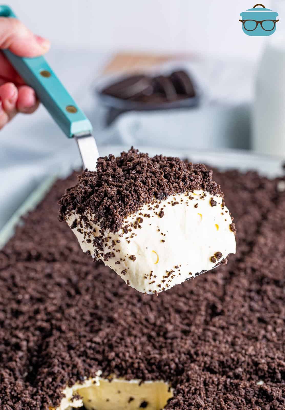 A serving of Oreo Dirt Cake being held by a serving utensil above the rest of the cake.