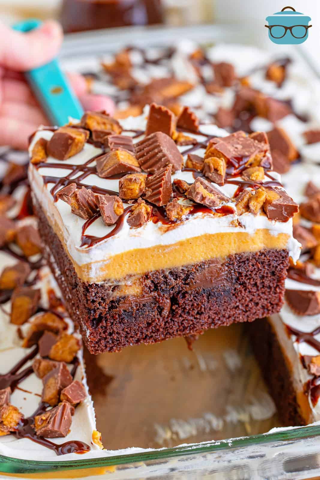 A serving utensil holding a large slice of Reese's Peanut Butter Poke Cake.