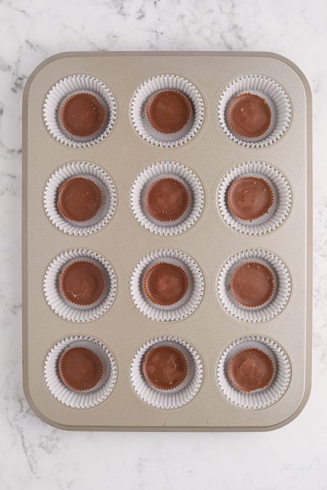 A muffin tin, each well lined with cupcake wrappers and a Reese's cup in each one.