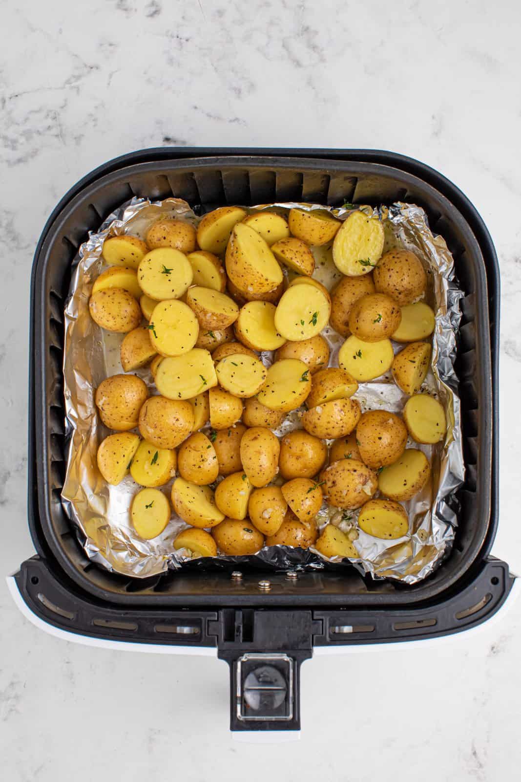 Seasoned potatoes in an Air Fryer basket lined with foil.