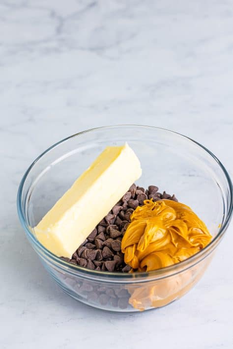 A glass mixing bowl with chocolate chips, peanut butter and salted butter.