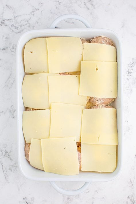 Swiss cheese on top of seasoned chicken breasts in a baking dish.