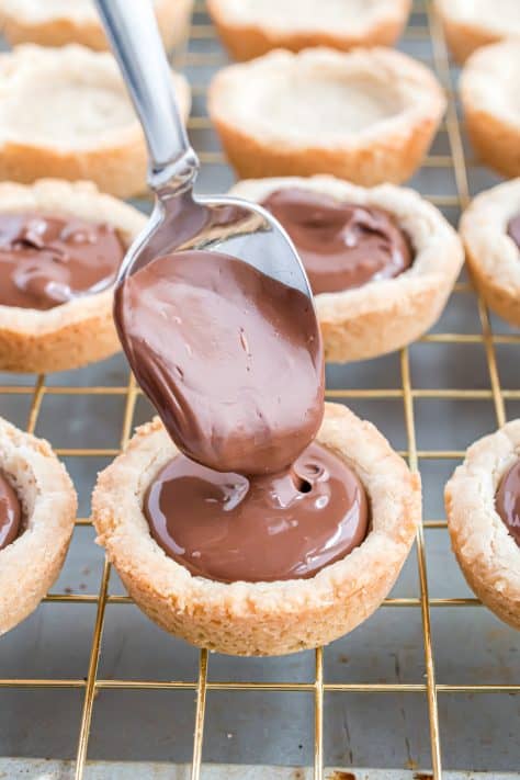 a spoon pouring melted chocolate into cookie cups.