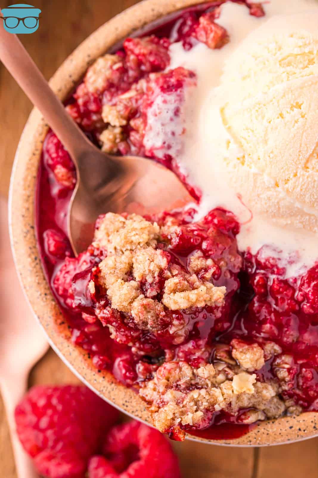 A spoon in a serving of Raspberry Crumble with vanilla ice cream on top.