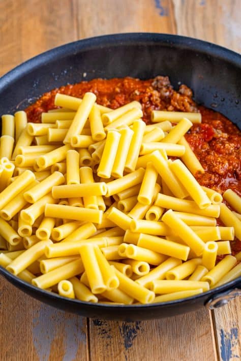 Cooked ziti pasta in a skillet with red sauce.