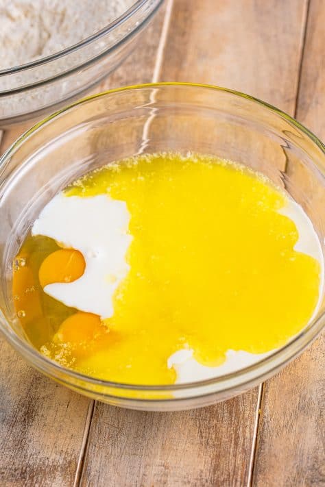 A glass mixing bowl with eggs, buttermilk, melted butter, and vanilla.