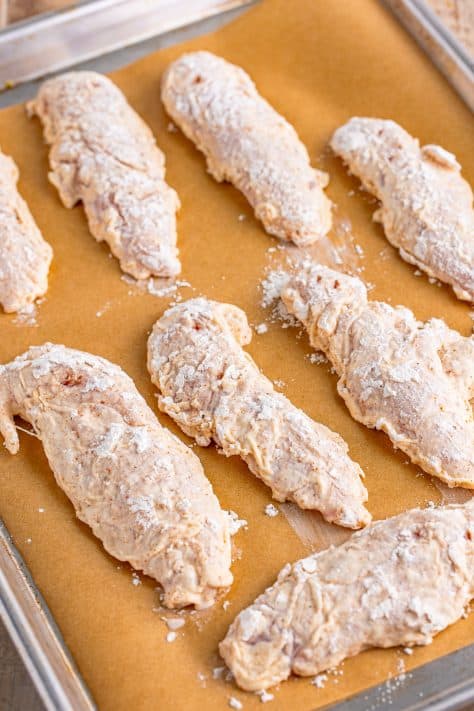 Flour coated chicken tenders on a parchment lined baking sheet.
