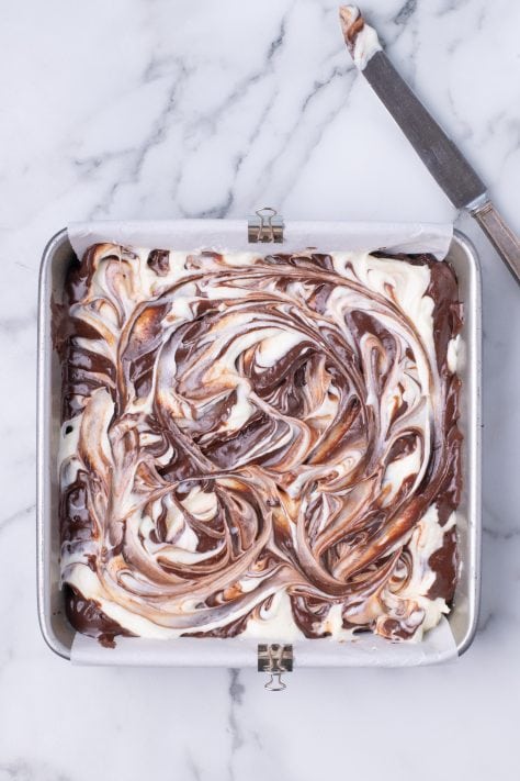 A marbled looking top of the brownie and cream cheese batter mixture in a baking pan.