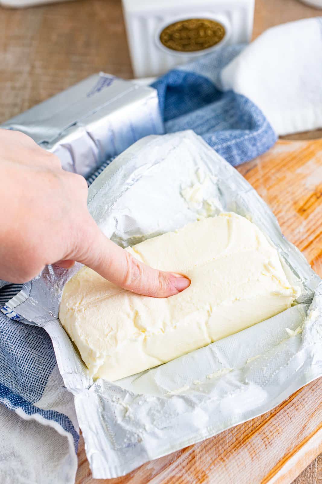 A hand squishing a block of Cream Cheese.