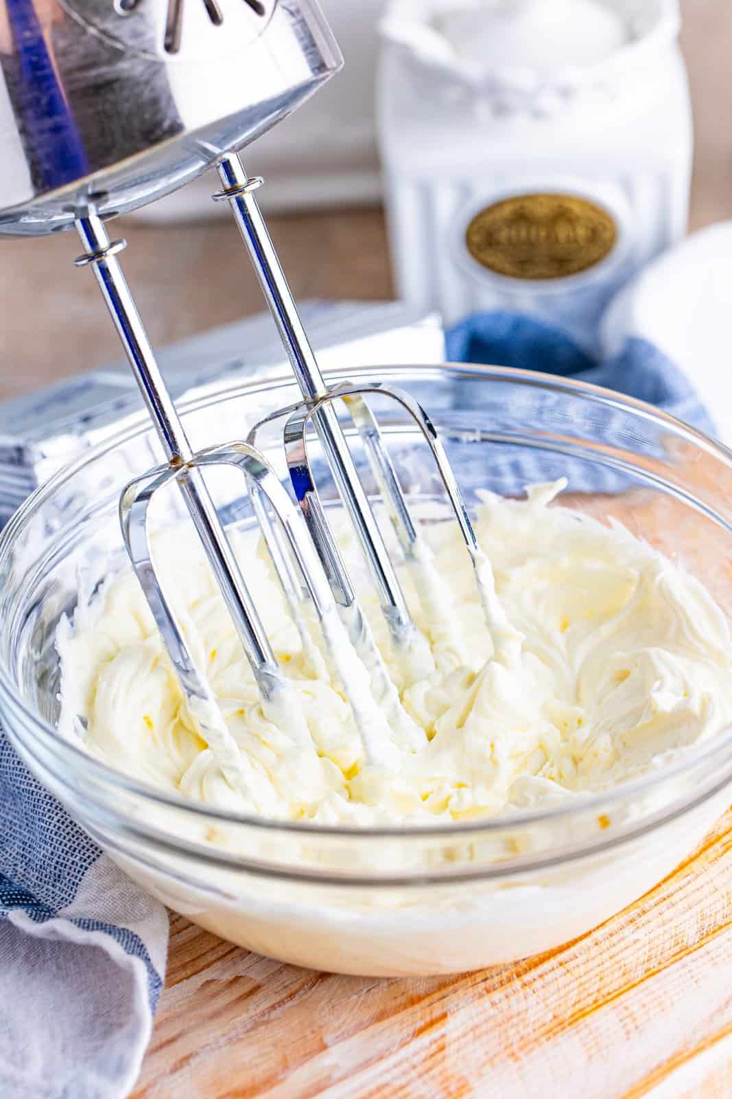 Electric mixer beaters in a glass bowl of softened cream cheese.