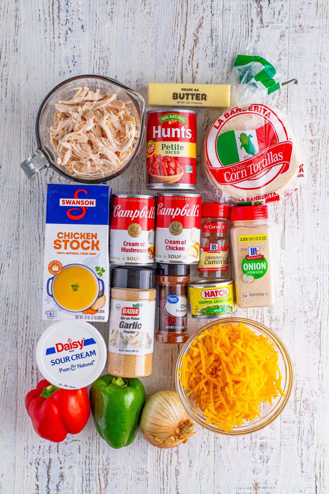 Rotisserie chicken, cream of mushroom soup, cream of chicken soup, petite diced tomatoes, green bell pepper, red bell pepper, cheddar cheese, butter, onion, chopped green chiles, chicken stock, sour cream, chili powder, garlic powder, ground cumin, onion powder, and white corn tortillas.