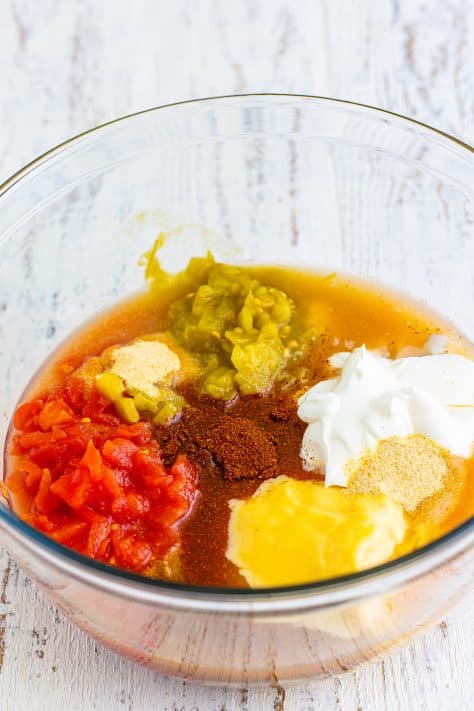 A mixing bowl with diced tomatoes, cream of chicken soup, cream of mushroom soup, chopped green chiles, chicken stock, sour cream, chili powder, garlic powder, cumin, and onion powder.