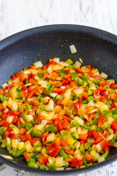 A skillet with melted butter, onion, green bell pepper, and red bell pepper.