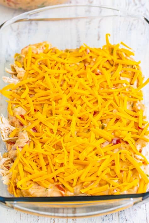 A baking dish with sauce, shredded chicken, and cheddar cheese in layers.