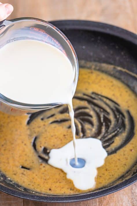 Milk being added to the skillet with flour, garlic powder, onion powder, pepper, salt, and melted butter.