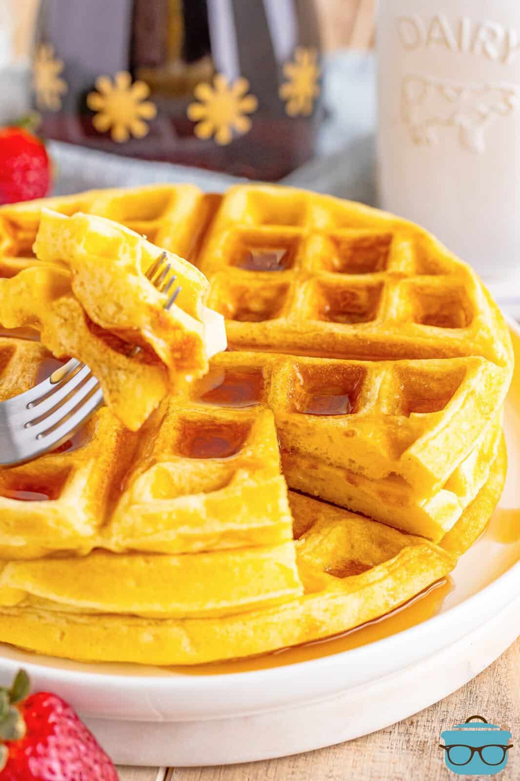 A fork folding a bite of buttermilk waffle above the stack of buttermilk waffles.