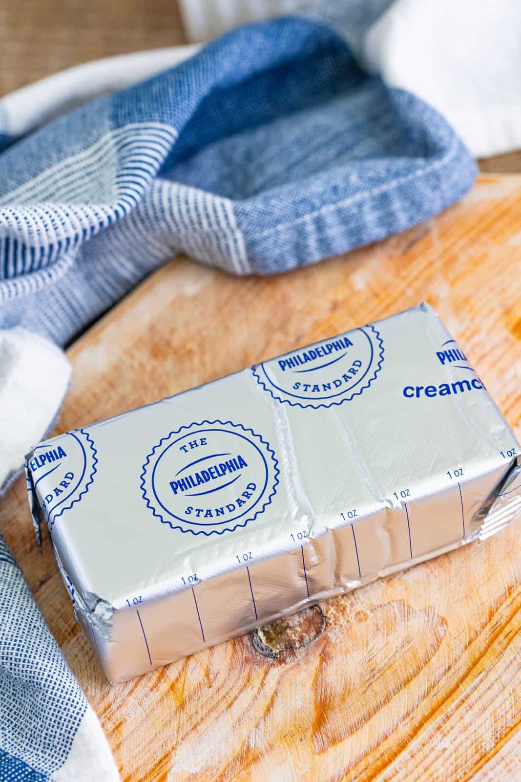 A wrapped up block of Philadelphia Cream Cheese sitting on the counter softening.