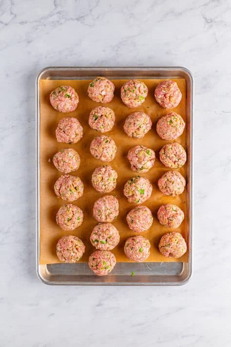 Uncooked meatballs on a lined baking sheet.