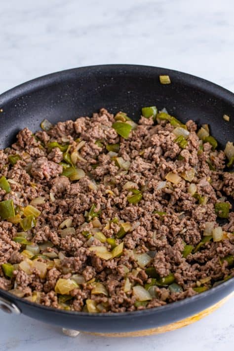 A skillet with cooked ground beef, onions, green bell pepper, garlic and melted butter.