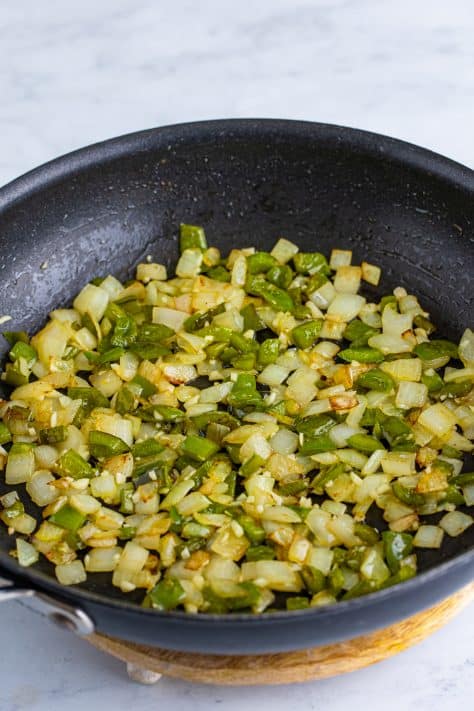 A skillet with melted butter, diced onion, diced bell pepper, and garlic.