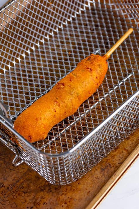 A fried Jalapeno Cheddar Corn Dog in a fryer basket.