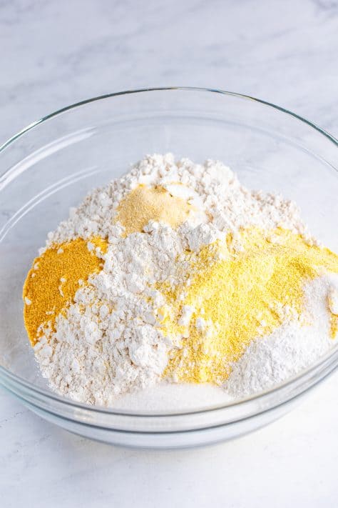 A mixing bowl with yellow cornmeal, flour, sugar, baking powder, garlic powder, onion powder, and salt.