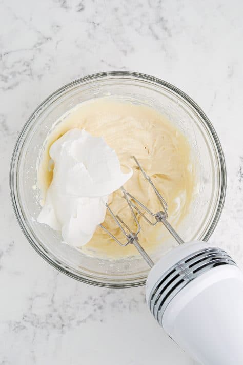 Whipped topping added to softened cream cheese, powdered sugar, caramel sauce and vanilla extract in a mixing bowl.