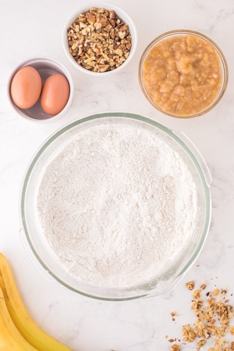 A large glass mixing bowl with cake mix, flour and baking powder.