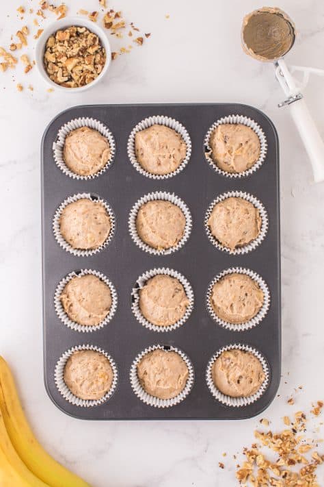 Banana Nut Cake Mix Muffin batter in cupcake liners in each of the muffin tin wells.