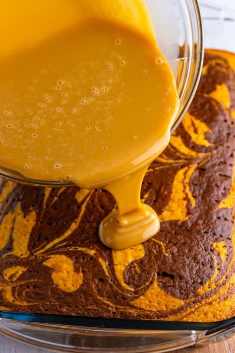 A bowl of caramel mixture being poured on a marbled cake.