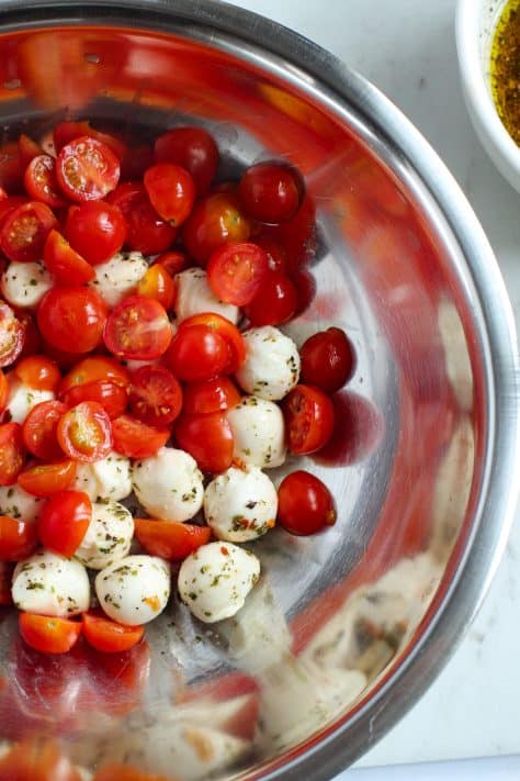 A large mixing bowl with cherry tomatoes cut in half and mozzarella balls.