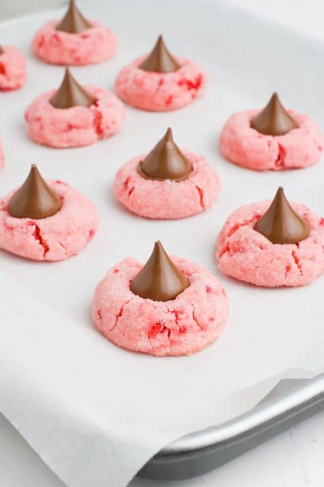 Hershey kisses being added to Cherry cookies on parchment paper.
