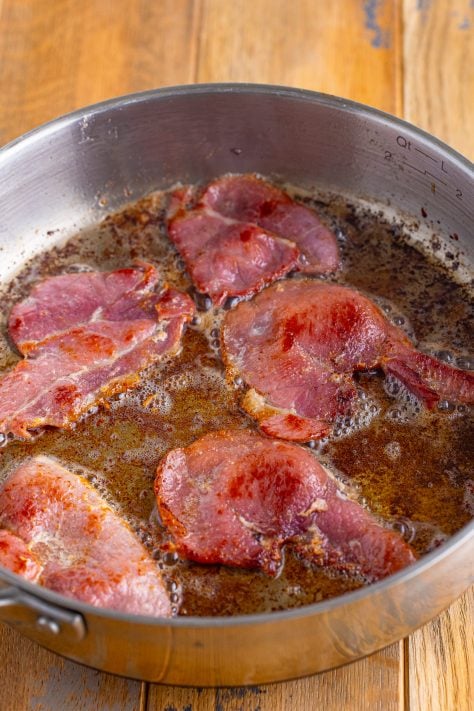 Ham cooking in melted butter in a pan.
