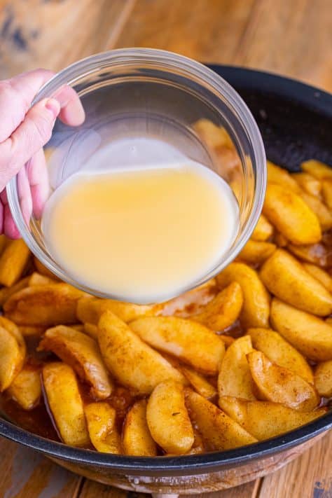 Cornstarch and apple juice being poured over the Fried Apples in a skillet.