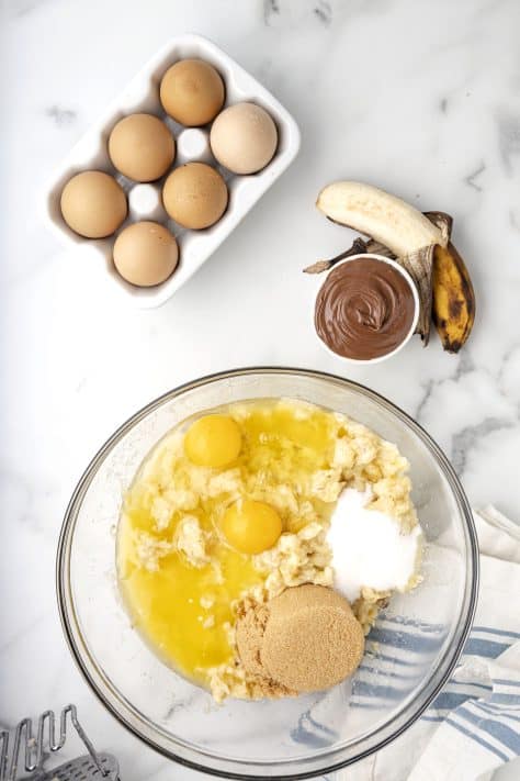 A glass mixing bowl with butter, bananas, brown sugar, sugar, eggs, and vanilla.