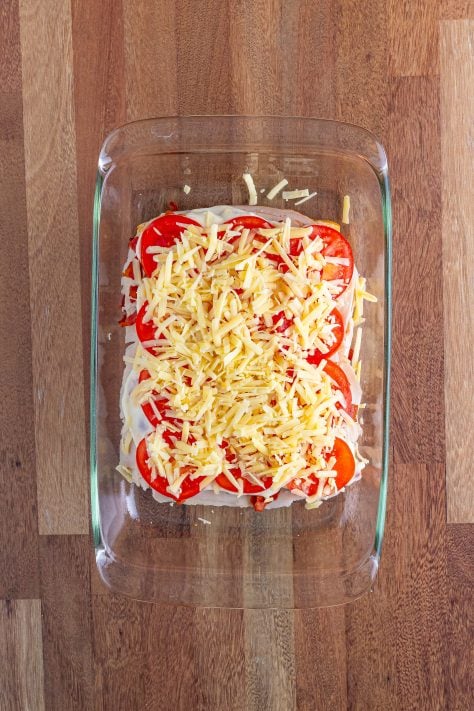 Shredded cheese on top of tomatoes and other fixins on a sandwich roll in a baking dish.